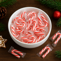 White bowl filled with red and white candy canes on a wooden surface with Christmas decorations.
