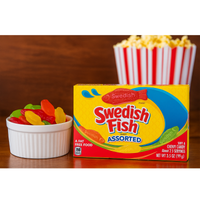 Box of Swedish Fish candy with a bowl of gummy fish and popcorn on a wooden surface.

